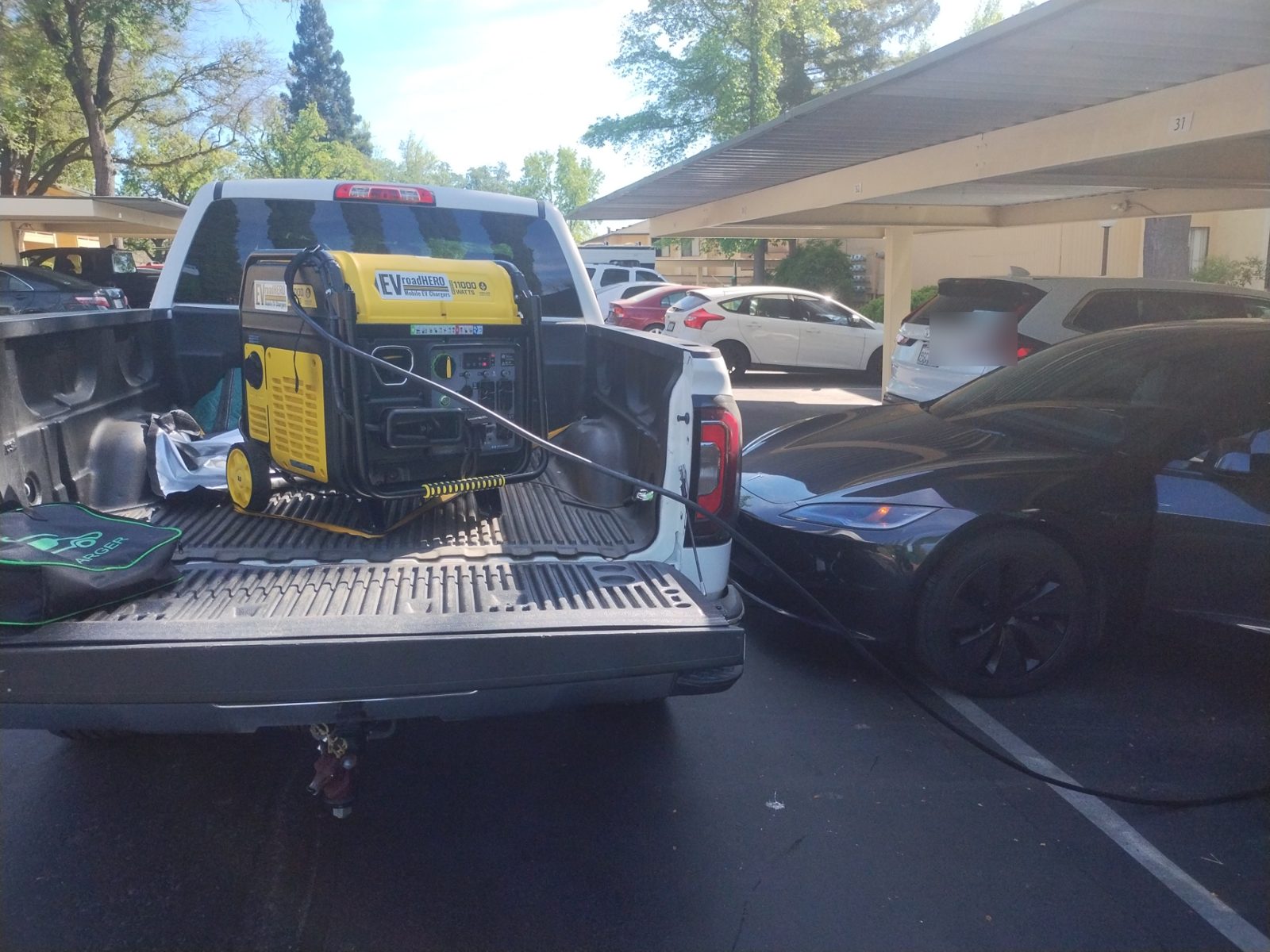 Black Tesla charging under an apartment carport from a mobile EV charging truck